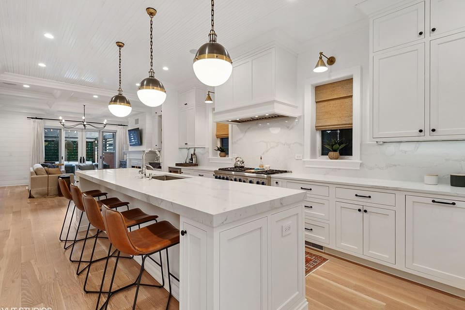 Elegant white kitchen with marble countertops and brown leather bar stools.