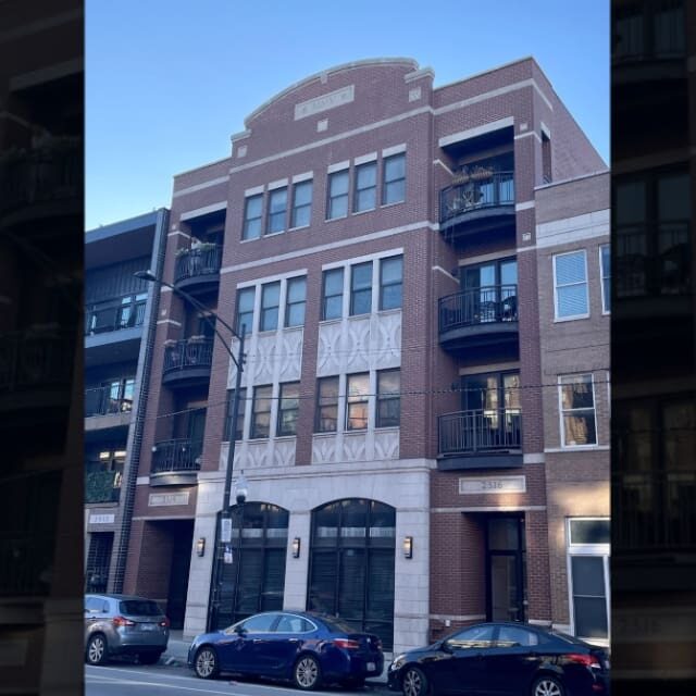 A multi-story brick apartment building with balconies and parked cars in front.