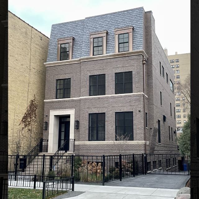 Modern three-story brick townhouse with black windows and a small front yard.